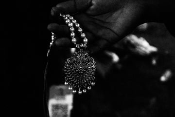 Close-up of a hand holding an ornate silver necklace