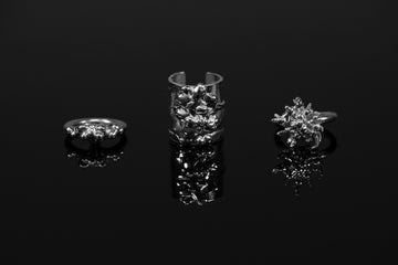 Three silver rings with organic textured surfaces on a reflective black surface