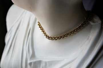 A gold chain necklace around the neck of a white classical statue bust